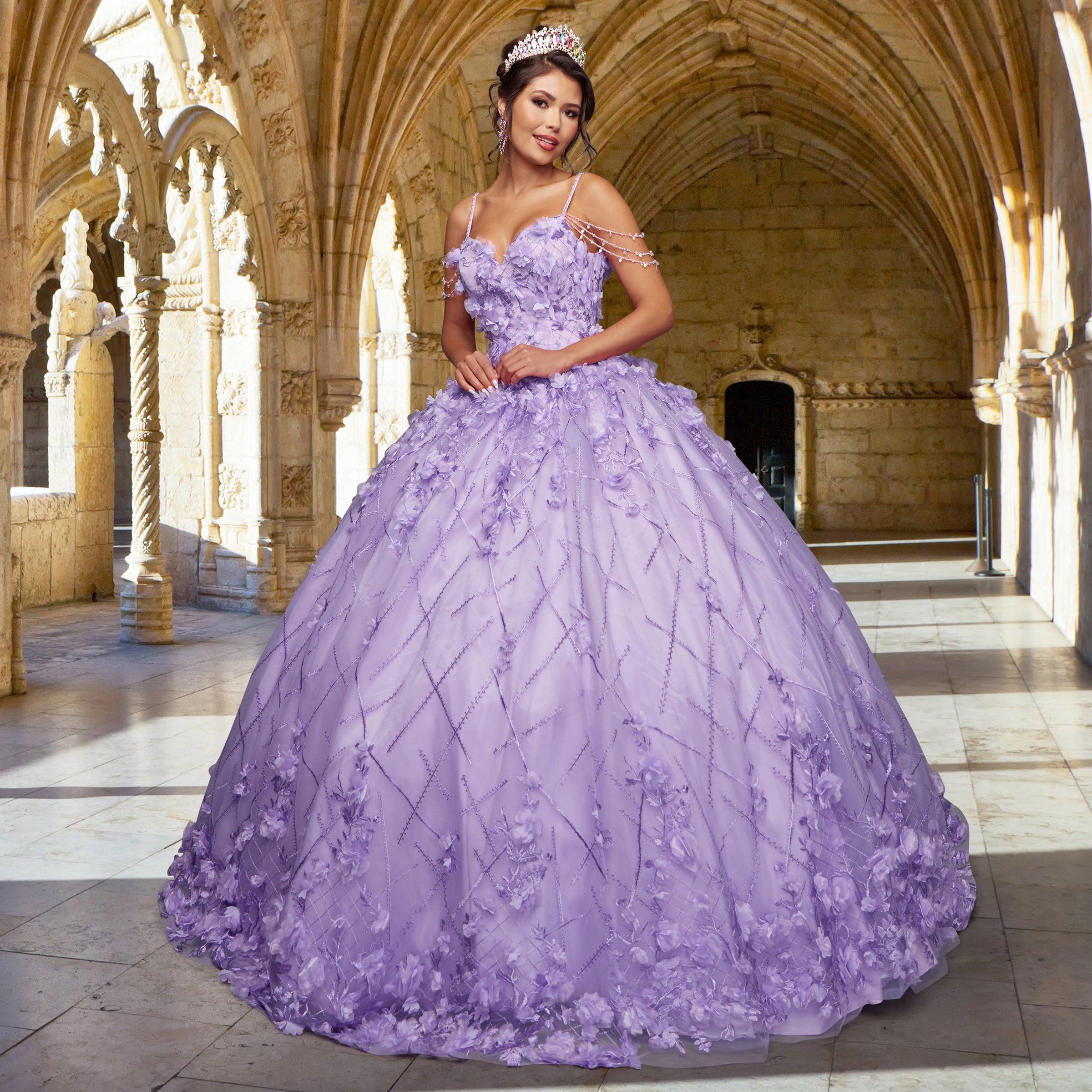 A woman wearing the Quinceañera Sample Dress QF105, a large ornate lavender cold-shoulder gown with a tiara, stands in an arched stone hallway featuring gothic architecture.
